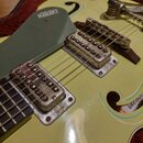 Detail světle žluté kytary s dvěma snímači a tmavě šedým pickguardem, na kterém je bílý nápis GRETSCH. Nástroj vykazuje známky opotřebení, zejména v…