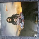 Fotografie znázorňuje obal učebnice s nápisy JOE SATRIANI GUITAR SECRETS a 41 PRIVATE LESSONS AS FEATURED IN guitar. Na snímku je zobrazen hudebník s…