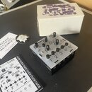 Bílé elektronické zařízení s nápisem DUDE a označením kanálů 1 CH až 5 CH. Přístroj má několik černých otočných ovladačů a přepínačů, na povrchu jsou…