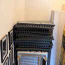 Stoh šedých akustických pěnových panelů s pyramidovým povrchem. Pod panely je umístěn rám s vlnitými pružinami a světlým potahem. Na fotografii nejso…