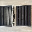 Otevřený transportní kufr s hliníkovým rámem a černým vnitřním polstrováním. V hlavní části je tmavě šedá egg-crate pěna, víko obsahuje svislé oddělo…