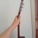 Fotografie zachycuje hmat krku a hlavy strunného nástroje z hnědého dřeva. Na hlavě jsou vidět tři stříbrné ladičky s bílými plastovými knoflíky. Žád…