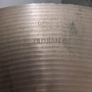Detail kovového povrchu činely s viditelným brusením. Na povrchu jsou vyraženy nápisy AVEDIS, ZILDJIAN, GENUINE a MADE IN USA. Nad textem je vidět ne…
