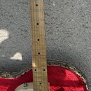 Elektrická kytara v krémové barvě s hmatníkem z jasného dřeva. Na hlavě je nápis Ibanez a modelové označení Deluxe 59 model. Nástroj má dva humbucker…