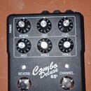 Černý kytarový předzesilovač s bílým předním panelem. Na panelu jsou šest otočných ovladačů s popisky REVERB, GAIN, LEVEL, BASS, MIDDLE a TREBLE, dva…