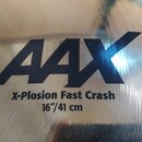 Detailní záběr na povrch mosazného činele. Na povrchu je černý nápis AAX a vedle něj text X-Plosion Fast Crash 16"/41 cm. Povrch vykazuje jemné konce…