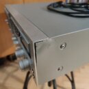 Stříbrný audio přístroj z kovu s ovládacími knoflíky na přední straně. V pravém horním rohu šasi je viditelný výrazný otlak a promáčknutí materiálu.…