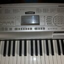 Stříbrný digitální klavír značky YAMAHA. Na ovládacím panelu jsou vidět nápisy STYLE, VOICE a MUSIC DATABASE s přehledy funkcí. V pravé dolní části p…