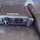 Černý bezdrátový mikrofonní systém značky LINE 6. Přijímač nese nápisy XD-V55 a 2.4 GHz VOCAL WIRELESS SYSTEM, dále obsahuje ovládací knoflík s čísly…