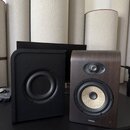 Dva studiové monitory umístěné na černém stole. Levý reproduktor je v černém provedení s černým membránovým hovorovým jednotkem. Pravý reproduktor má…