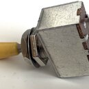 Fotografie znázorňuje elektrický přepínač s béžovým plastovým knoflíkem. Tělo přepínače je vyrobeno z kovu a obsahuje tři připájovací kontakty na zad…