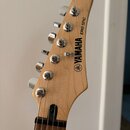 Fotografie zachycuje hlavu elektrokitary z přírodního světlého dřeva s chromovanými ladicími kolíky. Na hlavě je černý nápis YAMAHA, pod ním logo zna…