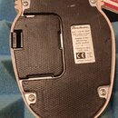 Fotografie zachycuje spodní stranu efekt pedálu s černým texturovaným povrchem. Na bílém štítku je uveden název značky Danelectro a text: „Batt: 1 x…