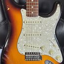 Elektrická kytara s korpusem v barevném přechodu od tmavě hnědé k žluté. Nástroj má bílý perleťový pickguard, tři snímače s bílými plastovými kryty a…