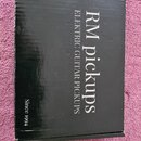 Černá papírová krabice s bílými nápisy. Na vrchní části je uveden text RM pickups a pod ním ELEKTRIC GUITAR PICKUPS. V levém dolním rohu je nápis Sin…