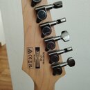 Zadní strana hlavy kytary z jasného dřeva se šesti černými ladicími mechanismy. Na dřevě jsou čitelné nápisy RG421AHM, 1P-05 a MADE IN INDONESIA. Ved…