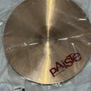 Kruhový činel z mosazného kovu v zlatavé barvě, který je zabalen v průhledné plastové fólii. Na povrchu je červeným písmem nápis pAiste a pod ním men…