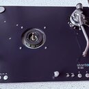 Černý gramofon s kovovým raménkem a stříbrným spodním rámem. Na povrchu je bílý nápis stanton a pod ním označení ST.150. V levé dolní části jsou tlač…