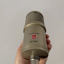 Kondenzátorový mikrofon v béžovém nebo zlatavém kovovém provedení s mřížkou v horní části. Na těle je uveden nápis LAUTEN AUDIO, červeno-bílé logo ve…
