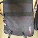 Černý textilní obal na hudební nástroj s dvěma vodorovnými popruhy a zipovou kapsou. V pravém dolním rohu je bílo-červený nápis GUITAR CASES. Na levé…