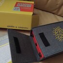 Žlutá krabice s nápisy „dreadbox“, „KOMO REBI FLANGER CHORUS“ a „WARM & DREAMY“. Vedle ní je šedý látkový obal s žlutým logem a nápisem „dreadbox“, u…