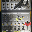 Žlutý mixážní pult značky APEX s označením modelu MIX100. Horní panel obsahuje různé vstupy a výstupy, včetně konektorů pro mikrofony, linkové vstupy…