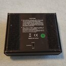 Fotografie zachycuje zadní stranu černého, hranatého elektronického zařízení. Na povrchu je nalepený štítek s nápisem CAUTION a rozsáhlým textem v an…