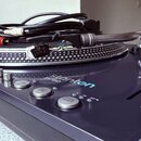 Černý gramofon s nápisem stanton a označením ST 150. Na talíři je umístěna hlava s nápisem stanton 500-II. Na přístroji jsou vidět tlačítka s nápisy…