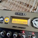 Detailní pohled na šedý kytarový pedál s nápisem LINE 6 a označením JM4 Looper. Zažhavený displej zobrazuje text STYLE BANK 005 a ATOMIC PUNK. Zaříze…