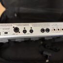 Záběr na zadní panel stříbrného elektronického zařízení s řadou konektorů. Jsou zde viditelné nápisy: POWER, RRC2 OUT, OUT-MIDI-IN, AMP CONTROL 1 a 2…