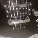 Detailní pohled na černou elektrickou kytaru. Viditelný je snímač typu humbucker s nápisem ESP designed a kovový kobylník. Povrch nástroje je černý s…