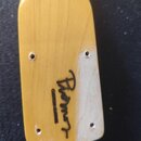 Fotografie zachycuje zadní část dřevěné hlavy kytary v přirozené žluté barvě. Na povrchu je černý nápis „Rodnor“ a pod ním menší text „CUSTOM GUITARS…