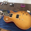 Elektrická kytara s těllem v žlutém odstínu a červeným bokem, vybavená dvěma humbuckery. Na hmatníku jsou vidět trojúhelníkové vložky a na těle čtyři…