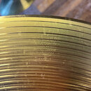 Detailní pohled na povrch mosazného činele s koncentrickými drážkami. Na povrchu je vyražen nápis SABIAN a pod ním menší nápis MADE IN CANADA. Povrch…