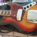 Elektrická basová kytara s korpusem v červeno-žlutém sunburst provedení a hnědým dřevěným povrchem. Nástroj má tmavý pickguard s texturou želvy a chr…