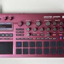 Kovový sampler v červenělesklé barvě s nápisy electribe sampler, MUSIC PRODUCTION STATION a KORG. Zařízení obsahuje displej, několik otočných knoflík…