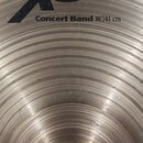 Detailní pohled na kovový činel stříbrné barvy s koncentrickými rýhami. Na povrchu je černý nápis „XS 20“ a pod ním text „Concert Band 16"/41 cm“. V…