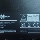 Fotografie detailu štítku s technickými specifikacemi na černém povrchu. Štítek obsahuje logo Gear4music a nápisy: INPUT POWER: 220-240VAC, 50/60Hz,…