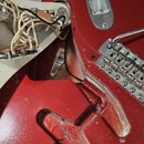 Fotografie zachycuje zadní část červené elektrické kytary s odstraněným krytem elektroniky. V dutině je vidět zapojení vodičů a potenciometrů, v doln…