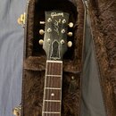Černá elektrická kytara v hnědém plišovém pouzdře. Na hlavě nástroje je bílý nápis Gibson a pod ním kurzívou Les Paul s menším doplňkem SPECIAL. Hmat…