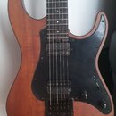 Elektrická kytara s hnědým dřevěným korpusem a černým pickguardem. Nástroj má dva humbuckery, jeden ovládací potenciometr hlasitosti a jeden tónu. Po…