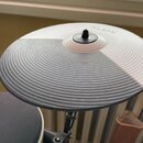 Kruhová elektronická činely s žebrovaným povrchem, rozdělená na bílou a šedou část. V horní části je bílý nápis Roland. Povrch vykazuje drobné známky…