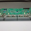 Fotografie zachycuje vnitřek elektronického zařízení, pravděpodobně zesilovače. Je vidět zelená základní deska s osazenými součástkami a čtyři hliník…