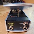 Fotografie znázorňuje VOLUME PEDAL v černo-stříbrném provedení s kovovým šlapadlem. Na černém předním panelu jsou nápisy VOLUME PEDAL, TUNER, IN a OU…