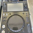 Černý DJ multifunctional player značky Pioneer DJ, model XDJ-700. Zařízení má v horní části displej a pod ním velký ovládací jog s černým povrchem. N…