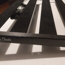 Černý pedálboard s povrchem z černého plstěného materiálu a kovovým rámem. Na přední hraně rámu je bílý nápis Harley Benton a logo s raketou. Nástroj…