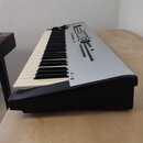Stříbrošedý digitální klavír s černými plastovými bočními panely. Na korpusu je viditelné logo a nápis "Kurzweil". Ovládací panel obsahuje displej, n…