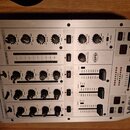 Stříbrný DJ mixér s nápisy BEHRINGER a VMX 100. Na horní části jsou ovládací prvky pro MAIN OUT, OUT A a OUT B, vpravo je vidět logo XPO. Přístroj ob…
