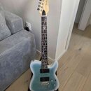Elektrická kytara s modrým přechodovým povrchem těla a hnědým hmatníkem. Na hlavě je viditelné logo Fender. Hmatník obsahuje bílé dekorativní vložky…