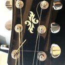 Fotografie zachycuje hlavu černé akustické kytary s chromovanými ladičkami. V horní části je bílý nápis YAMAHA a uprostřed se nachází dekorativní orn…